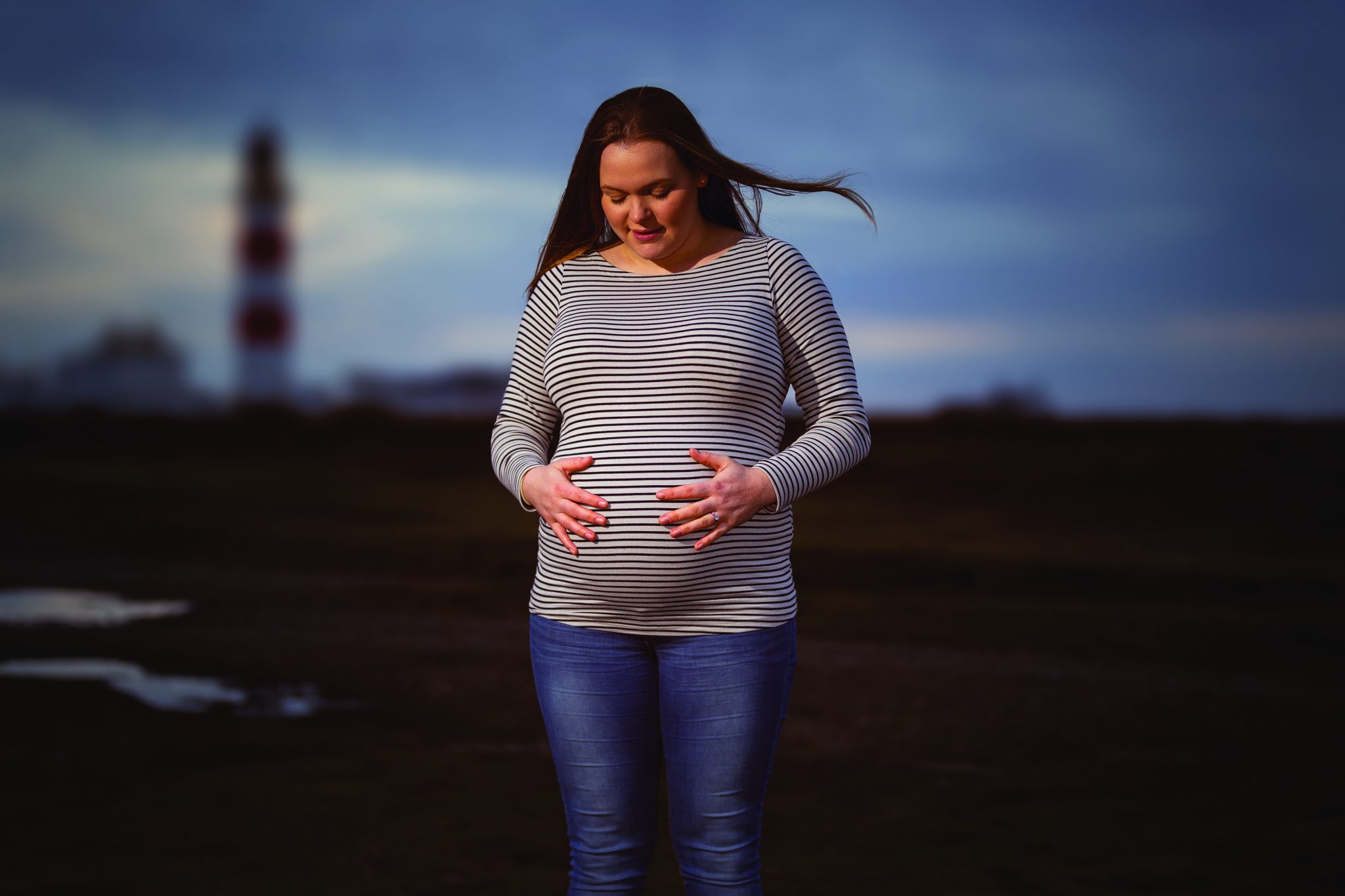 Pregnant women holding stomach near lighthouse